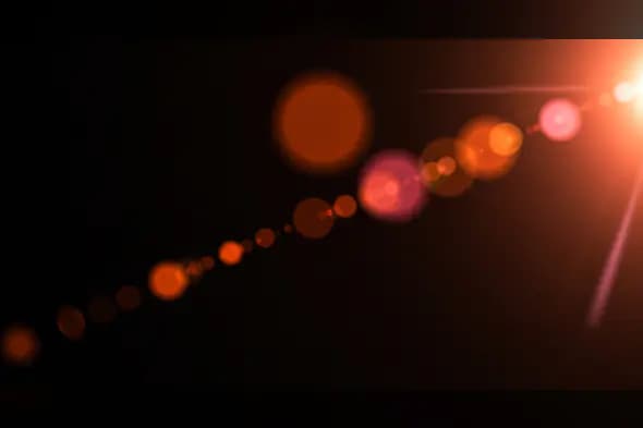 Warm Orange Lens Flare Burst with Circular Bokeh Trail on Black Background