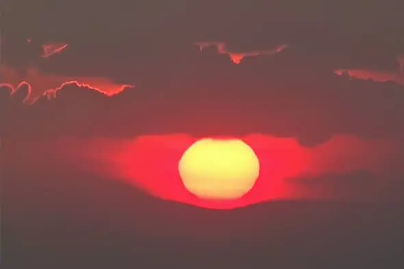 Dramatic Red Sunset with Glowing Sun Through Cloudy Sky
