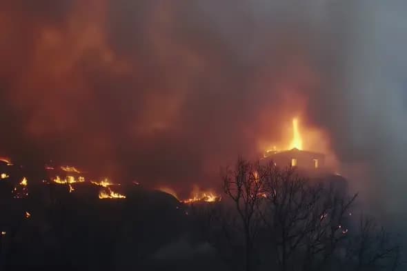 House Engulfed in Wildfire on Hillside at Night