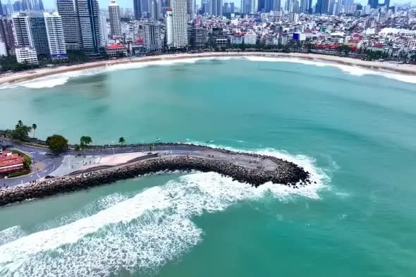 Aerial View of Urban Beach with Rocky Breakwater and Cityscape