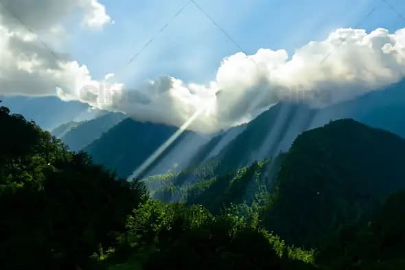 Sunlight Streaming Through Clouds Over Mountain Forest