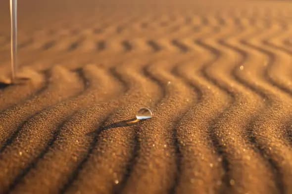 Golden Desert Sand with Water Droplet in Soft Sunset Light