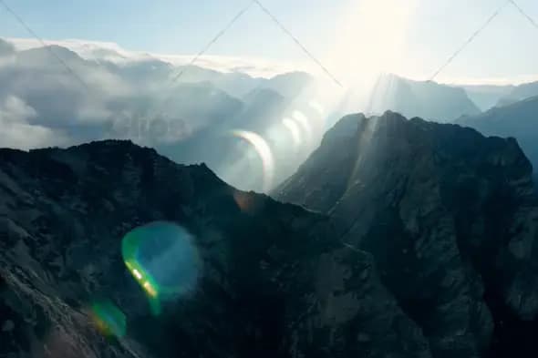 Aerial View of Sunlight Breaking Through Clouds Over Mountain Peaks
