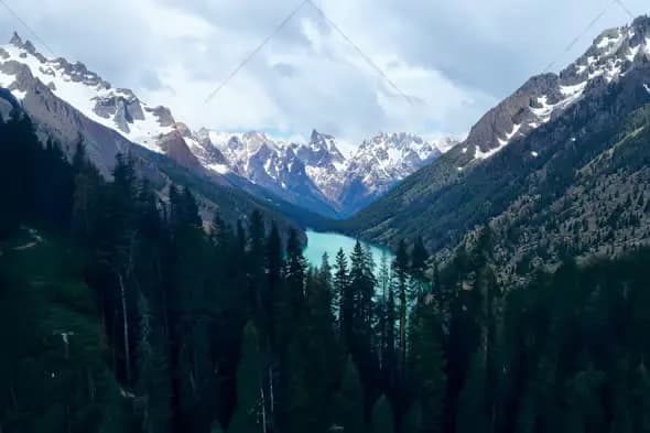 Aerial View of Mountain Lake Surrounded by Snow-Capped Peaks and Evergreen Forest
