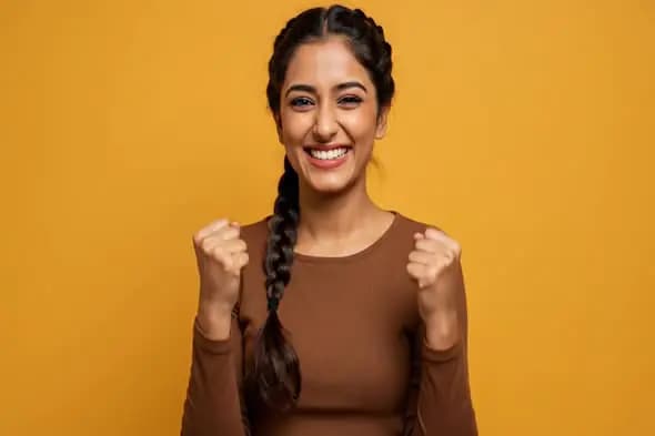 Joyful Indian Woman Celebrating Success with a Bright Smile on Yellow Background