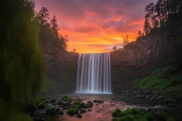 Majestic Waterfall Thunders Against Fiery Sunset Sky